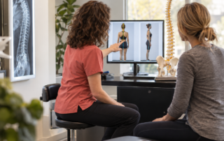Female chiropractor explaining posture assessment results to a patient at HAVEN Chiropractic in Asheville, NC, highlighting evidence based chiropractic care.